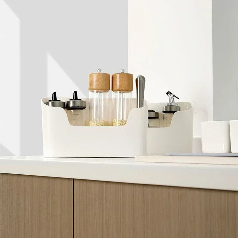 Two off-white storage caddies on a kitchen worktop holding oil bottles and wooden-topped spice grinders.