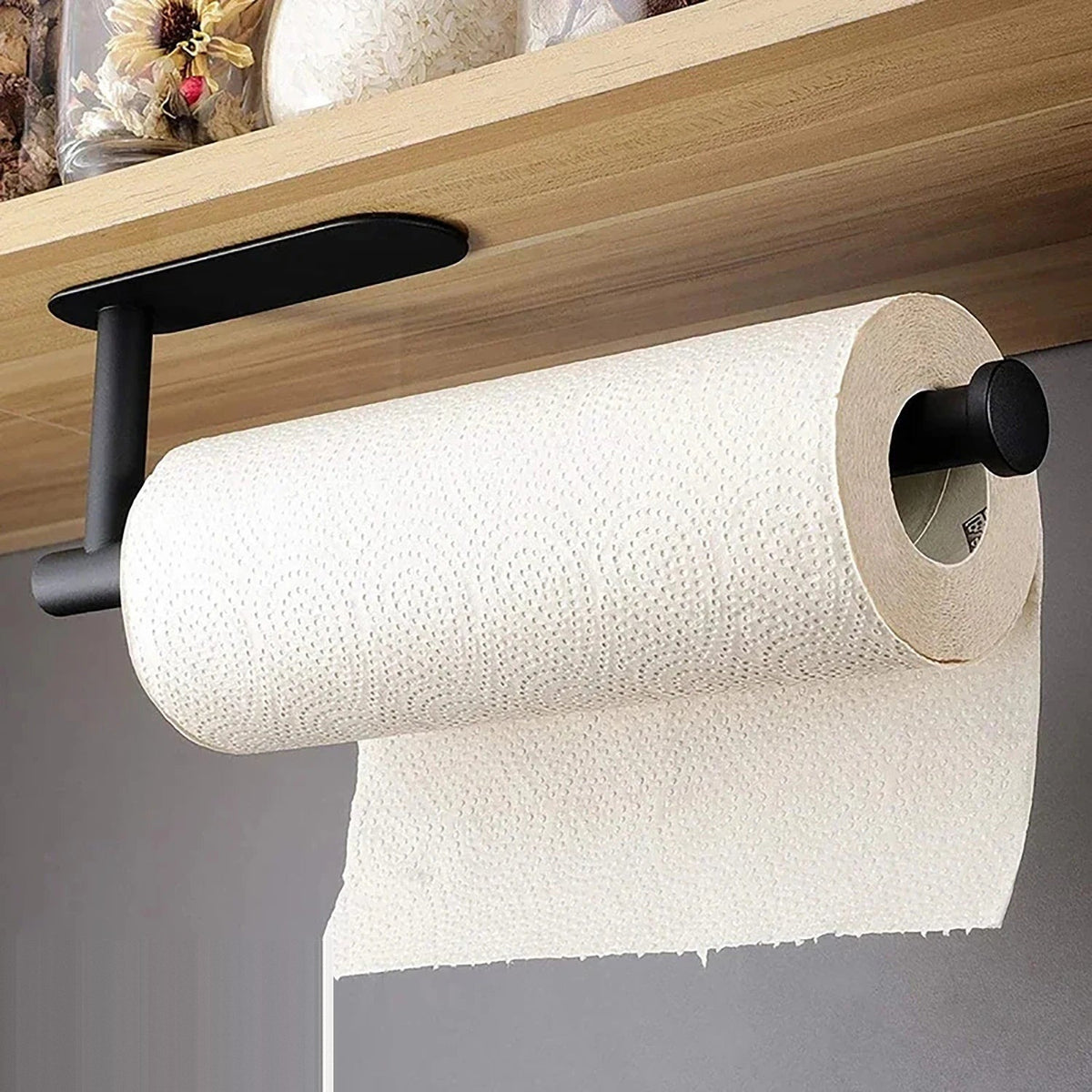 The large matt black roll holder fixed to the underside of a wooden shelf, holding a full kitchen roll with the end sheet hanging down.